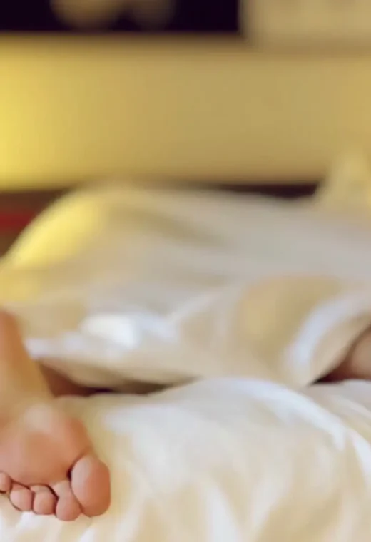 in image of someone in bed with their feet hanging out of the covers, showing a poor well-being in healthcare