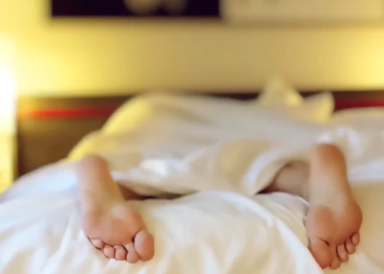 in image of someone in bed with their feet hanging out of the covers, showing a poor well-being in healthcare