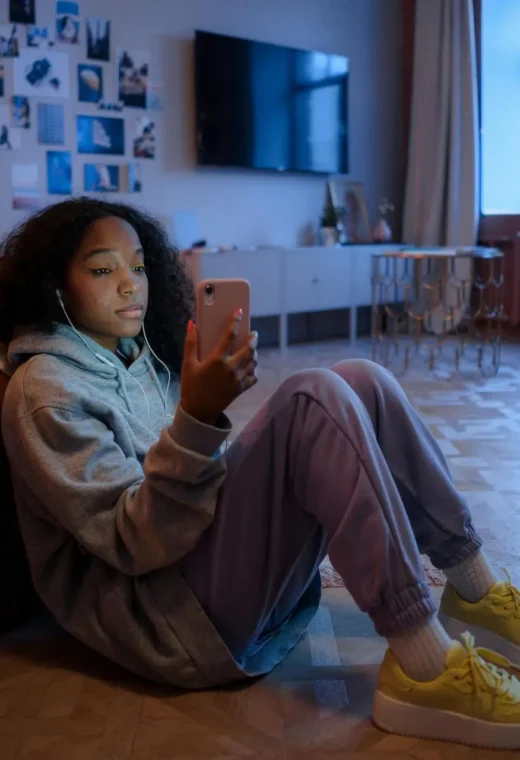 image of a girl sat on the floor leaning against a bed looking at her phone