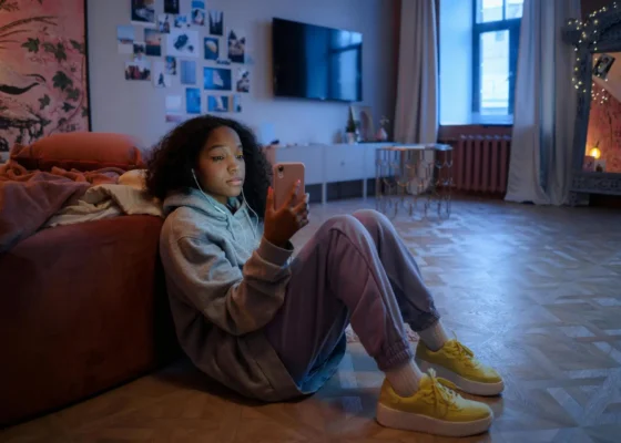 image of a girl sat on the floor leaning against a bed looking at her phone