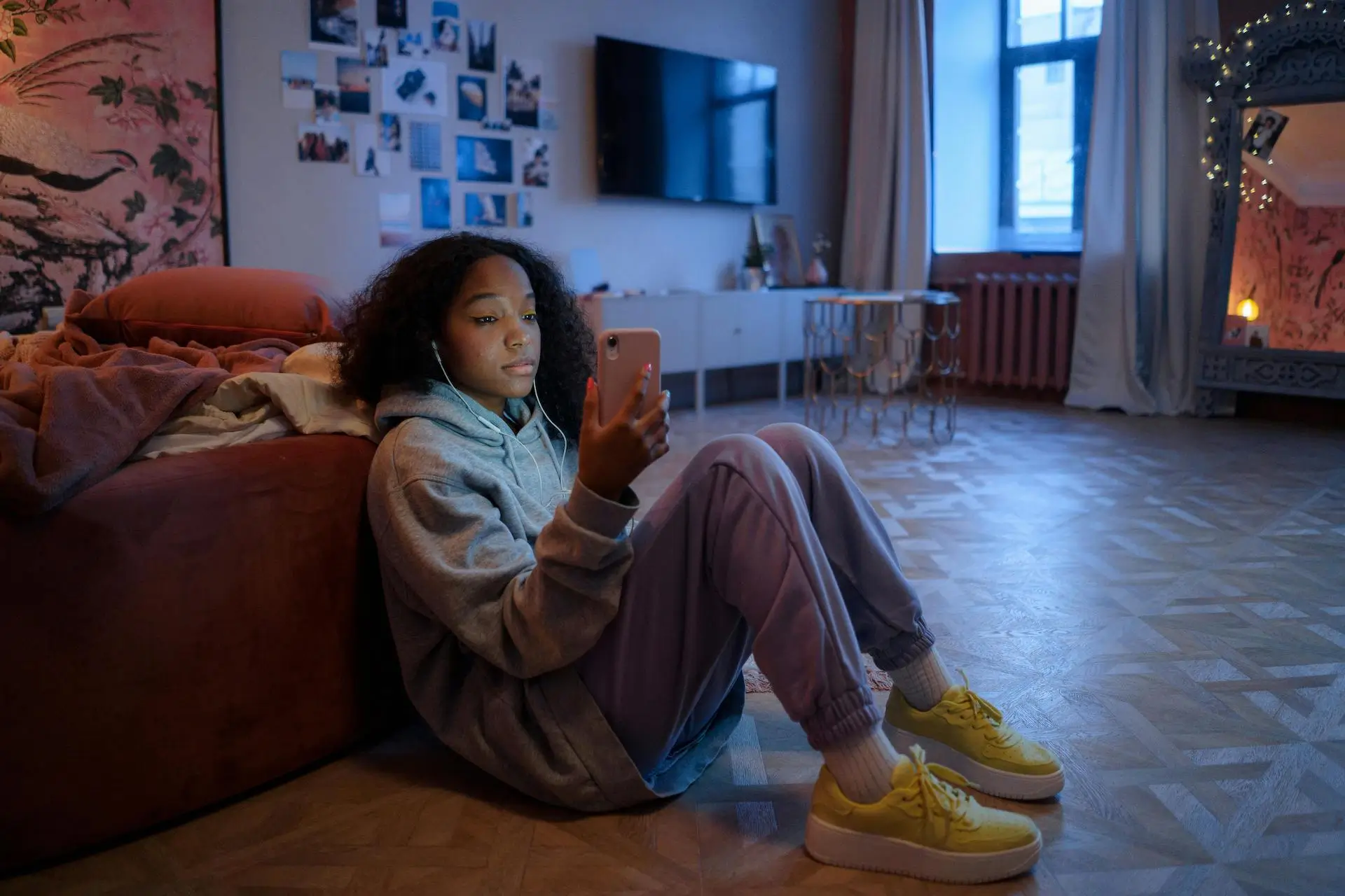 image of a girl sat on the floor leaning against a bed looking at her phone