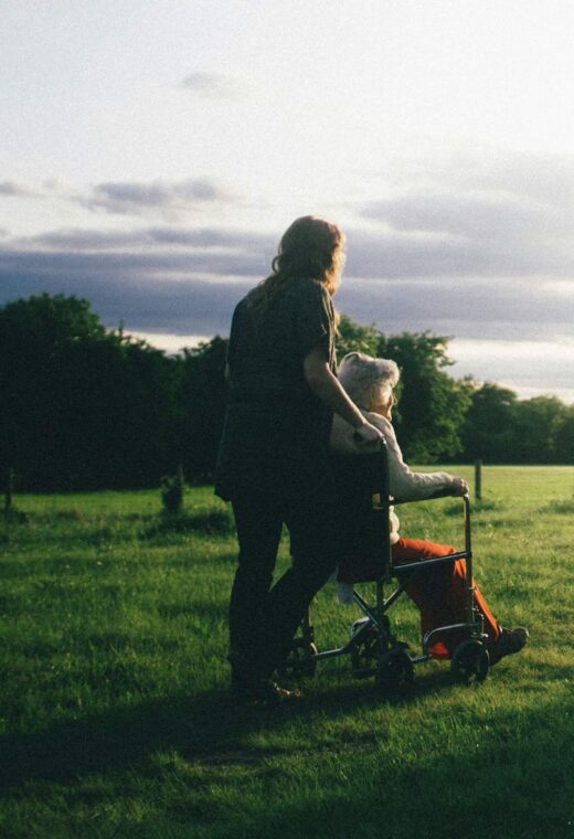 An image of a care worker and an elderly woman in a wheelchair in a field