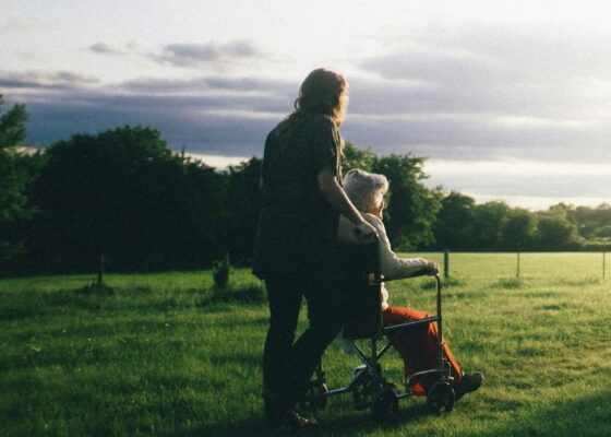 An image of a care worker and an elderly woman in a wheelchair in a field