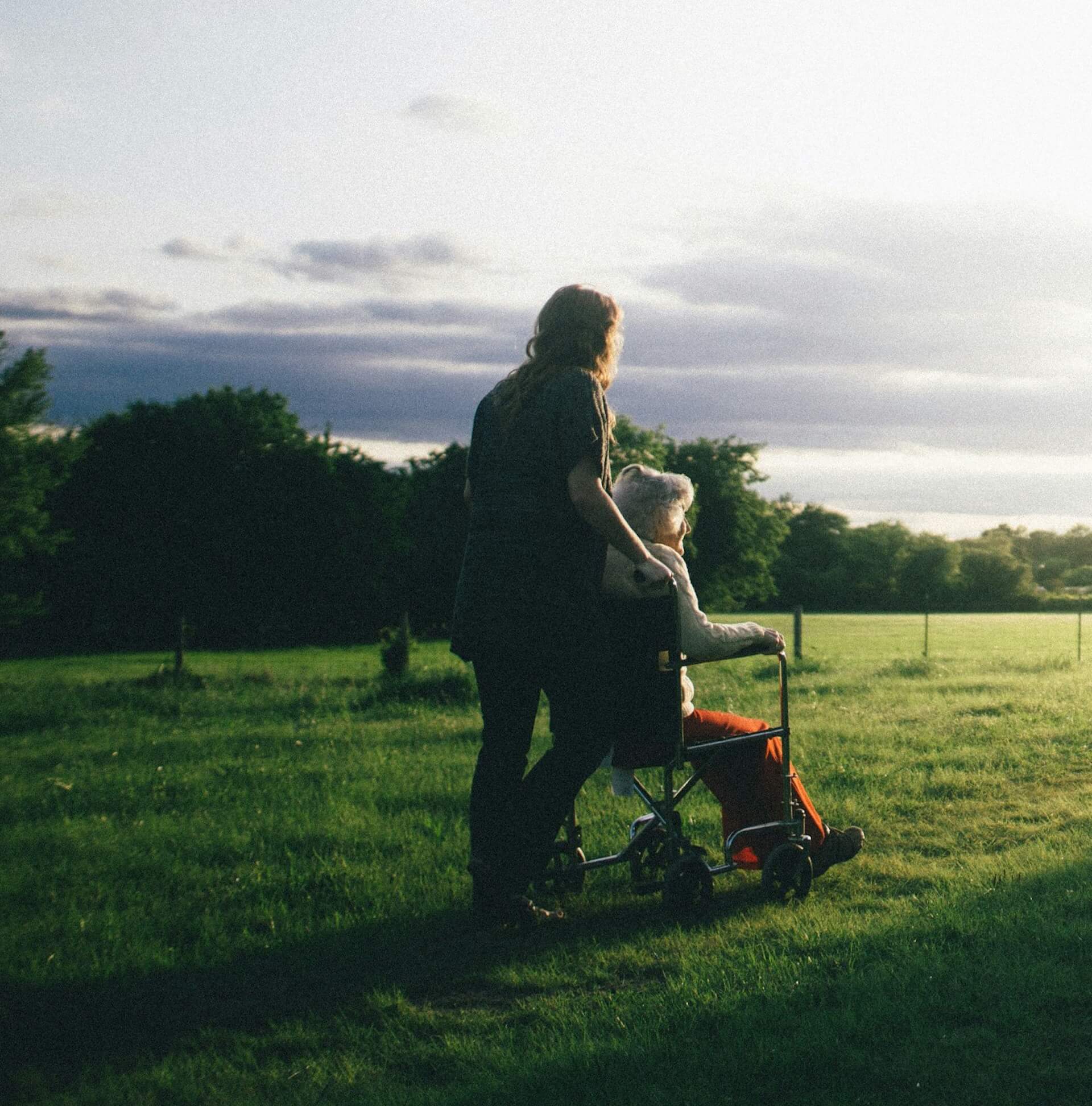 An image of a care worker and an elderly woman in a wheelchair in a field