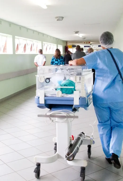 healthcare staff walking down a hallway in blue scrub suit with an incubator