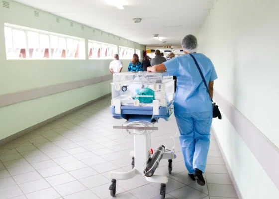 healthcare staff walking down a hallway in blue scrub suit with an incubator