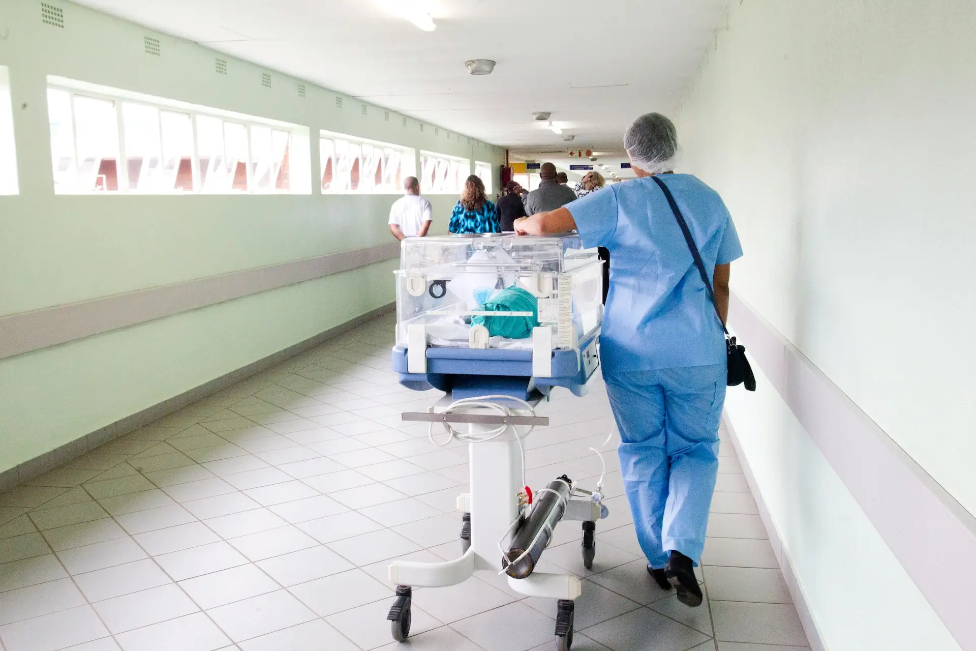 healthcare staff walking down a hallway in blue scrub suit with an incubator